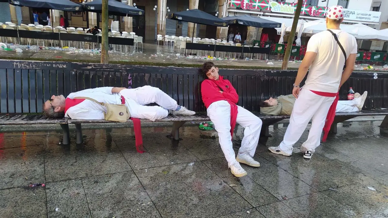 Un trío de amigos dormidos en un banco de la Plaza del Castillo bajo la mirada de su compañero. SERGIO DURÁN