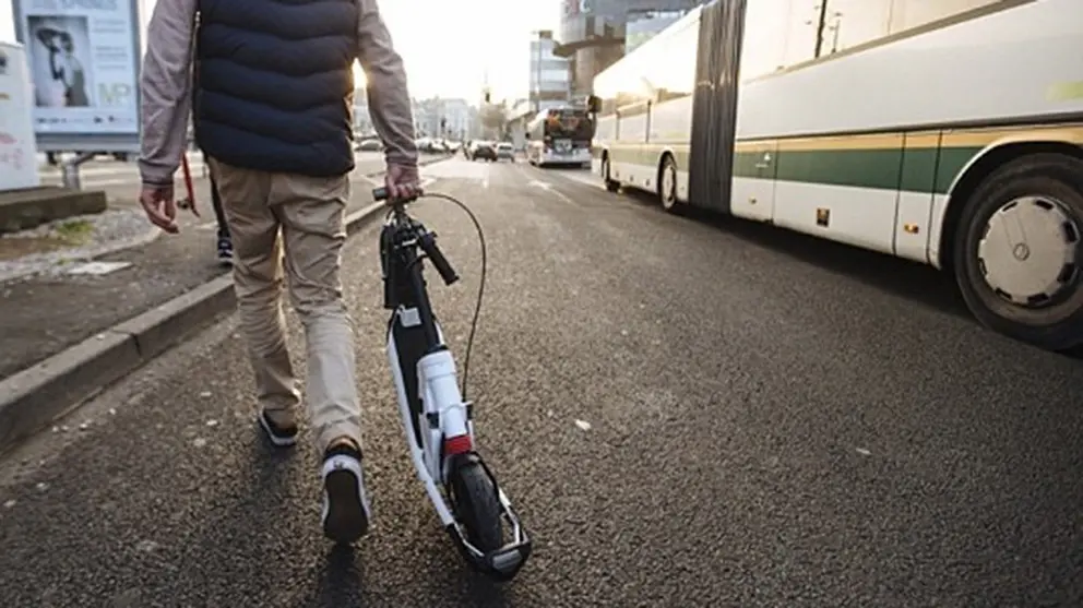 Imagen de un conductor de un patinete eléctrico caminando por la calle junto a un autobús urbano. ARCHIVO
